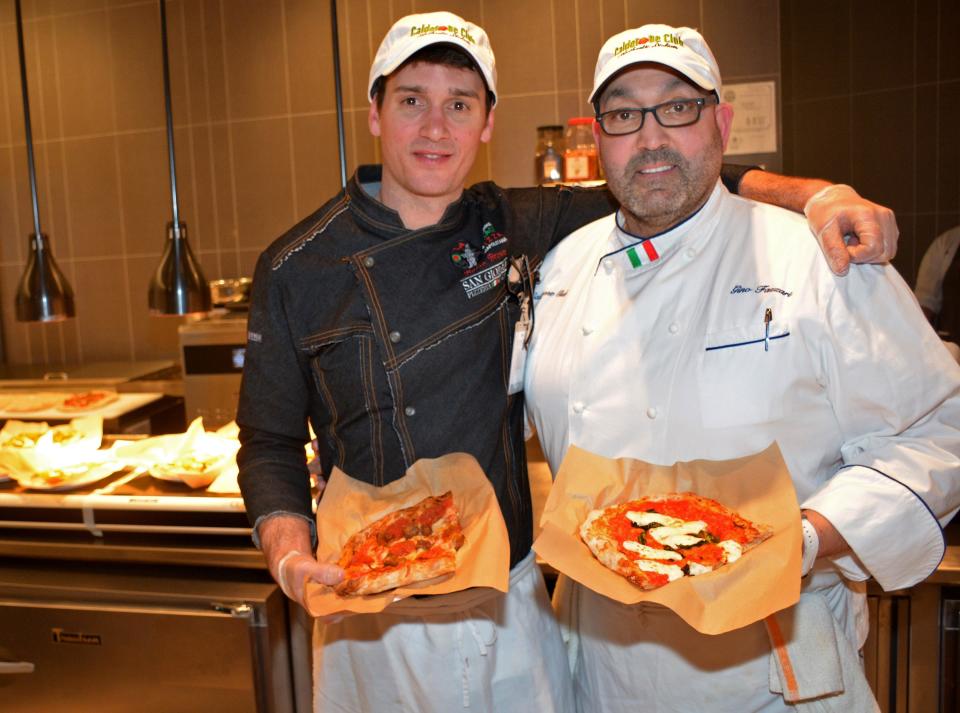 Calderone Club chef Robin Brown (left) and restaurant owner Gino Fazzari hold pizza slices at the restaurant-themed stand at Fiserv Forum. The stand opened this month.