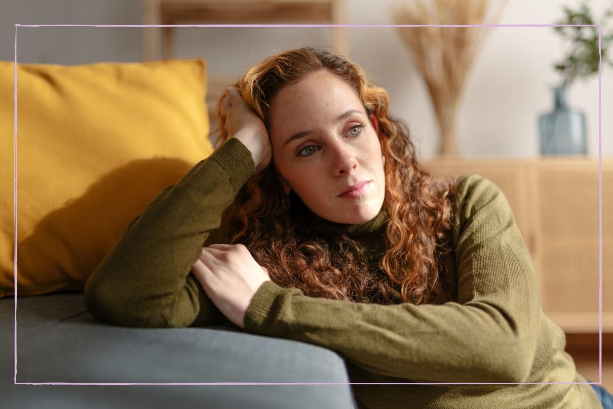  Woman leaning against sofa looking thoughtful. 