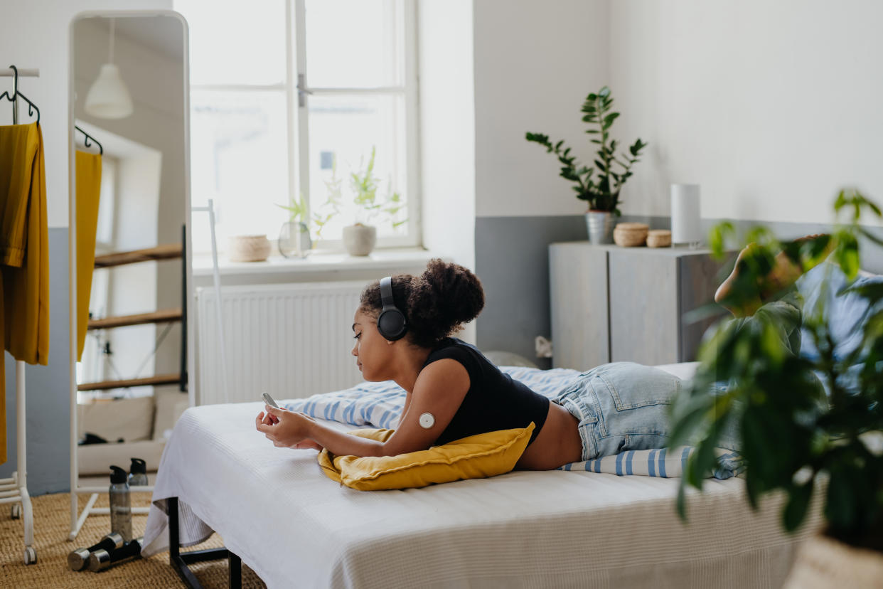 Sad teenage diabetic with insulin pump, lying on bed and scrolling on smartphone, feeling lonely and depressed. Teenage girl feeling different from friends, have body image issues because of insulin pump and CGM. Concept of daily routine of a teenage girl living with a chronic disease.