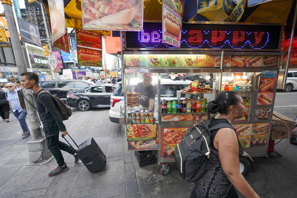 Pedestrians walk past Youssef Mohamed, center, working at his hot dog cart in New York's Times Square, Wednesday, Sept. 14, 2022. It's becoming clearer that New York City's recovery from the pandemic will be drawn out and that some aspects of the city's economic ecosystem could be changed for good. More workers returned to their offices as the summer ended. But those limited numbers mean continued hardship for New Yorkers whose jobs are built around the commuting class. (AP Photo/Mary Altaffer)