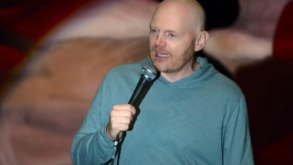 Bill Burr in an aqua pull over, holding a microphone.
