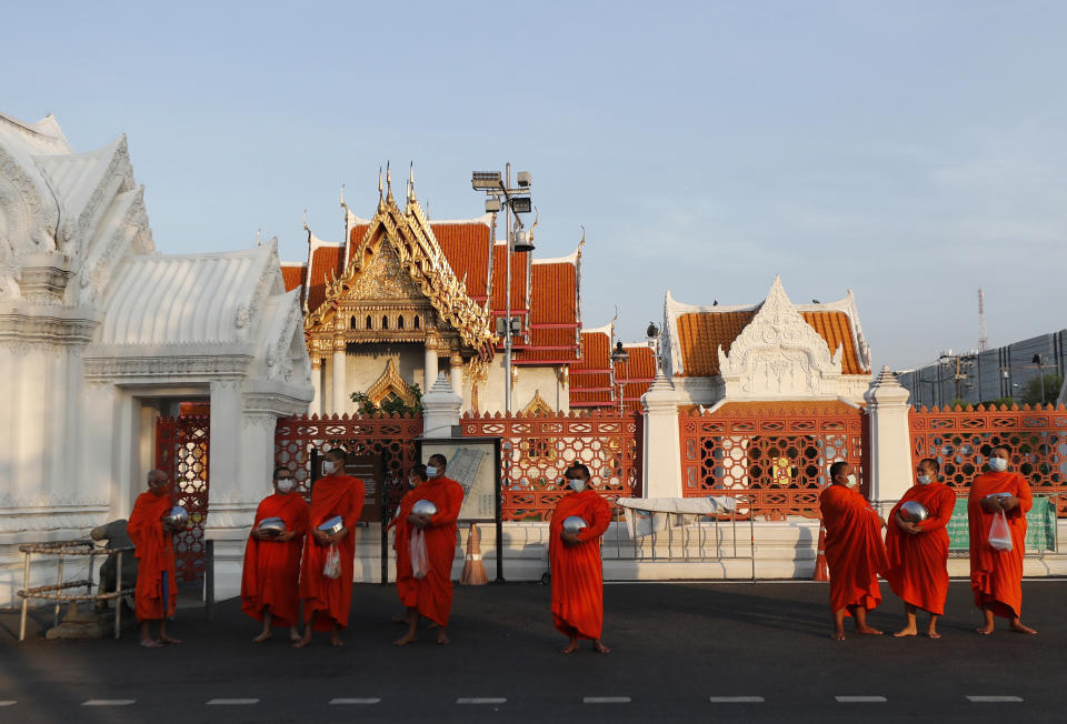 Buddhist monks wearing face masks to protect themselves from the coronavirus wait in line to receive alms during a morning alms offerings in front of Marble Temple in Bangkok, Thailand, Friday, April 16, 2021. (AP Photo/Sakchai Lalit)