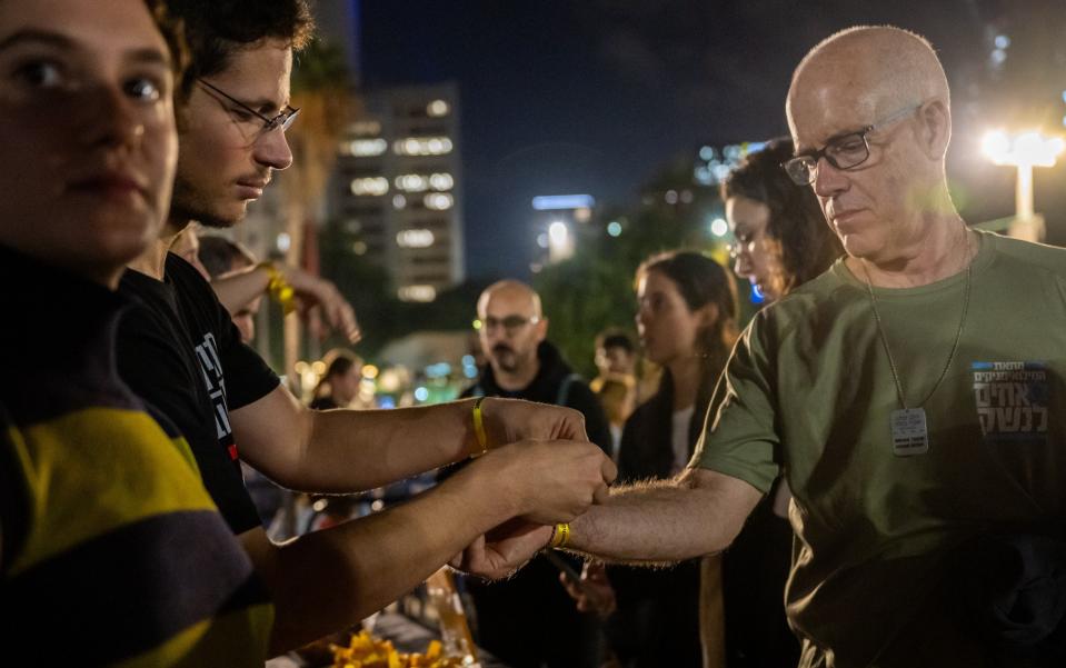 Volunteers tie yellow ribbons on demonstrators that read, "Oct 7. Bring Them Home Now" at a rally to demand that Israeli Prime Minister Benjamin Netanyahu secures the release of Israeli hostages