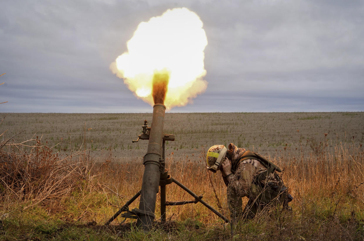 A Ukrainian National guard soldier crouches and covers his ears as an artillery piece blasts off a mortar.