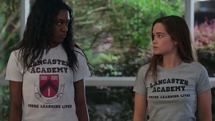 Two young women look at one another, both wearing high school T-shirts in a scene from First Kill on Netflix.