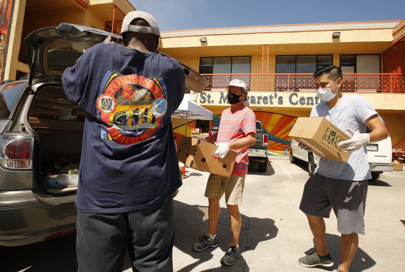 LOS ANGELES, CA - MAY 06: Roberto Calderon, left, and Ronson Chu, right, load a package of food at St. Margaret's Center Catholic Charities of Los Angeles as close to 300 families line up now each Wednesday to collect food at a drive-thru and walk-up pantry. The need for food has reached record levels in L.A. County and food banks are hustling to keep up. The Los Angeles Regional Food Bank has gone from serving 300,000 families to to 500,00 families per month. Some are now having to purchase or compete for food as supplies are running slow or they are struggling with a shortage of volunteers. Downtown on Wednesday, May 6, 2020 in Los Angeles, CA. (Al Seib / Los Angeles Times)