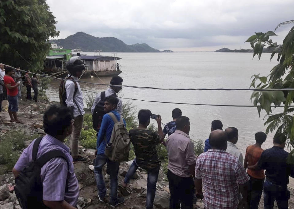 Passersby standing on the opposite bank watch rescuers