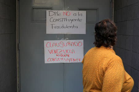 A woman walks past placards that read "Say no to the fraudulent constituent" (top) and "Closed. Venezuela does not want constituent" at the door of a school where the polling center will be established for a Constitutional Assembly election next Sunday, in Caracas, Venezuela July 24, 2017. REUTERS/Marco Bello