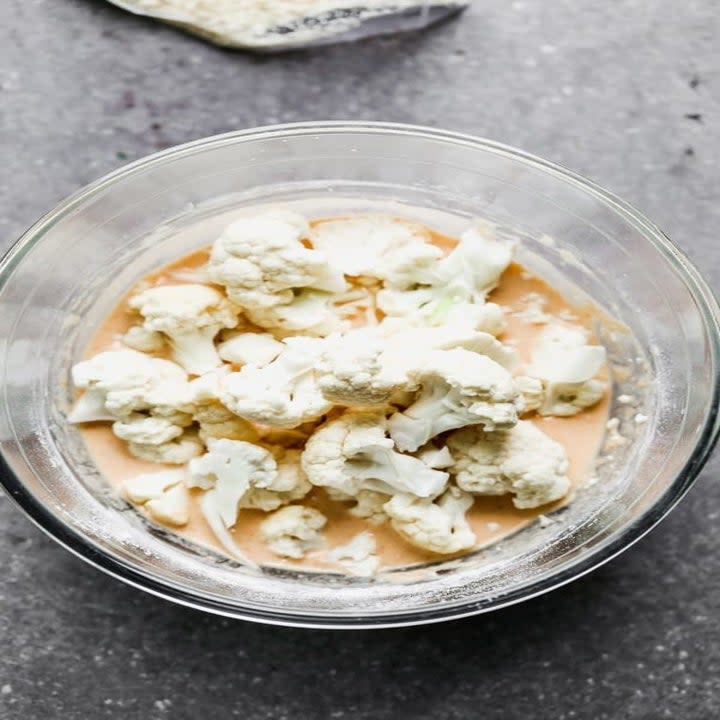 Cauliflower florets being dredged in a mixture of milk and buffalo sauce.