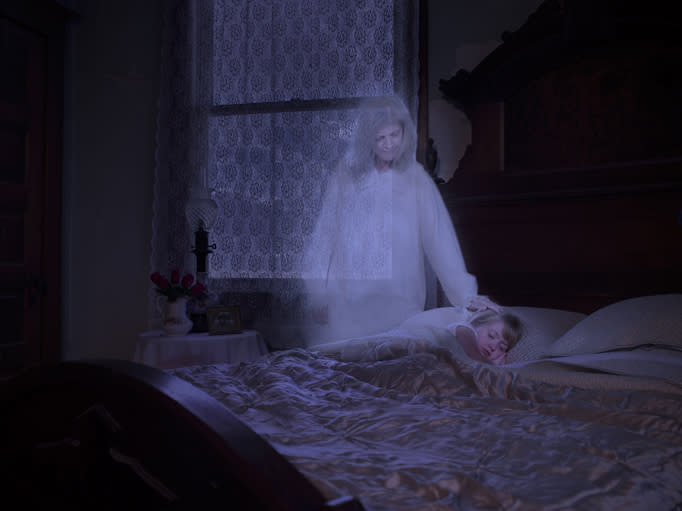 Transparent figure looms over sleeping person, suggesting a ghostly presence in a dimly lit room