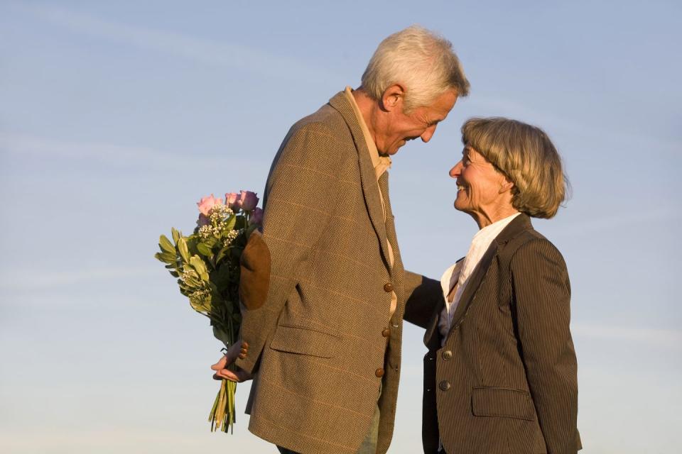 senior couple, man hiding bouquet, smiling, side view