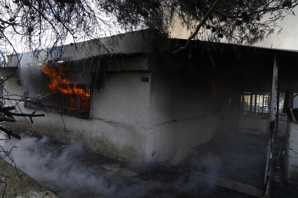 Flames and smoke comes out from the window of a house during a wildfire in Thea area some 60 kilometers (37 miles) northwest of Athens, Greece, Thursday, Aug. 19, 2021. A major wildfire northwest of the Greek capital devoured large tracts of pine forest for a third day and threatened a large village as hundreds of firefighters, assisted by water-dropping planes and helicopters, battled the flames Wednesday. (AP Photo/Thanassis Stavrakis)