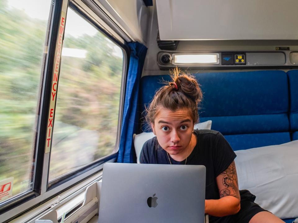 The author works on her laptop while sitting in the blue chair with a window on the left side