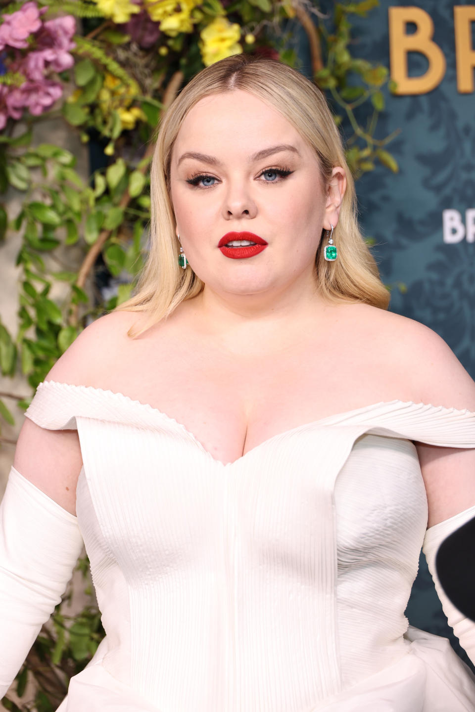 Nicola Coughlan on the red carpet, wearing a white off-the-shoulder gown with long gloves and green earrings