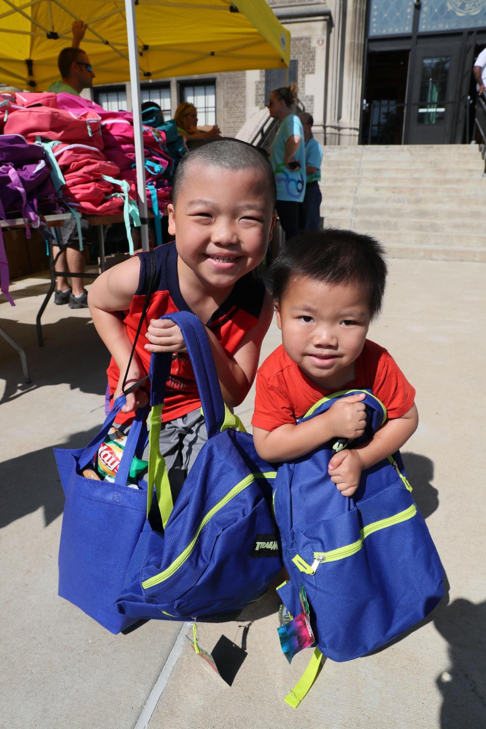 Elijah Vang age 9, left and his brother, Connor Vang age 3 pose with the free backpacks they were given at the event. City of Milwaukee Health Department annual health fair, being held  at Washington High School.  Another will be held August 9th at Journey House.  The community event provides school-required vaccinations for children without private health insurance, lead testing, and other health checks as well as other resources for students and fun activities.