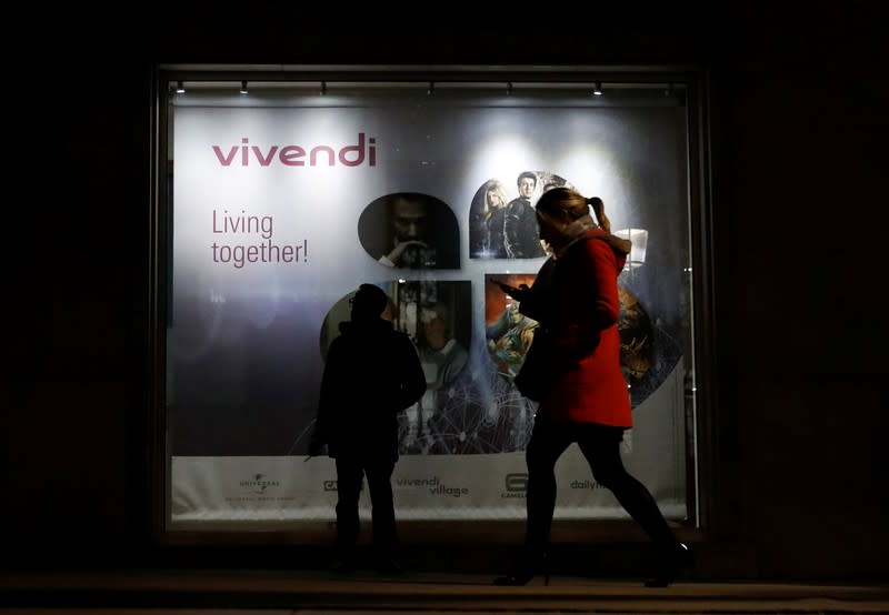 A man stands as a woman walks past a sign of Vivendi at the main entrance of the entertainment-to-telecoms conglomerate headquarters in Paris