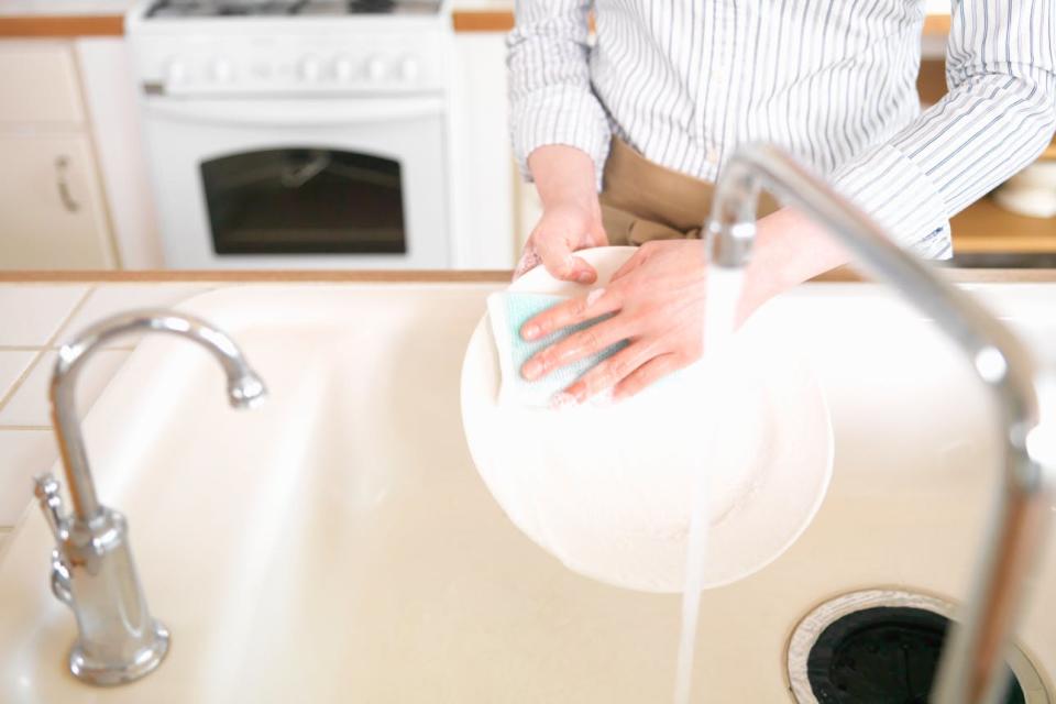 A woman washes a plate with a sponge in the kitchen sink
