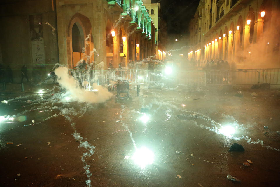 Anti-government protesters throw firecrackers against the riot police, background, during a protest near the parliament square, in downtown Beirut, Lebanon, Sunday, Dec. 15, 2019. Lebanese security forces fired tear gas, rubber bullets and water cannons Sunday to disperse hundreds of protesters for a second straight day, ending what started as a peaceful rally in defiance of the toughest crackdown on anti-government demonstrations in two months. (AP Photo/Hussein Malla)