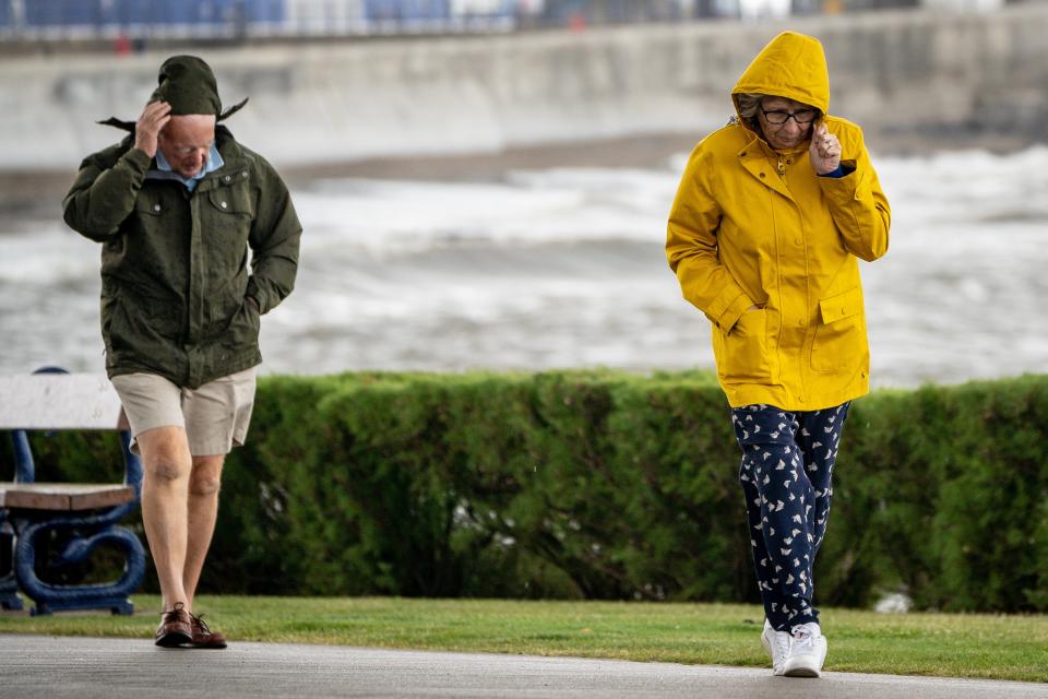 People pull down their hoods to shelter from the wind as they walk along the sea front in Porthcawl, Wales (Ben Birchall/PA). (PA Wire)