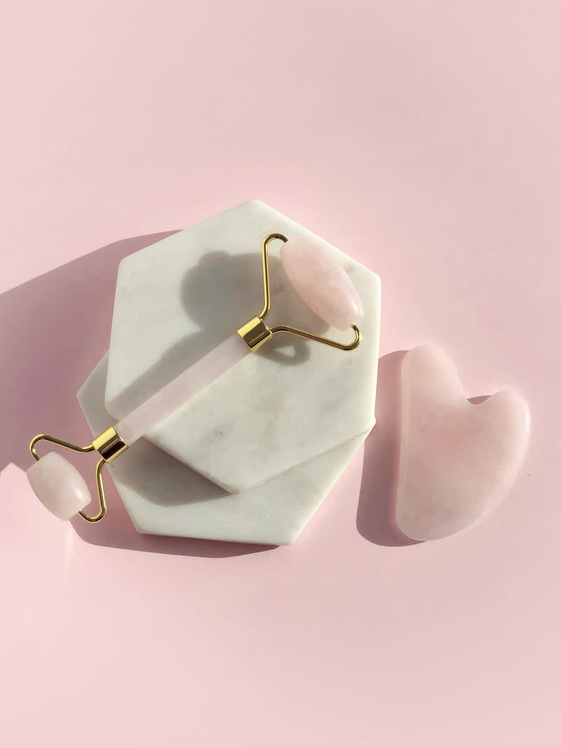 On a pink background is shown a block of Rose Quartz Gua Sha and the Rose Quartz Face Roller, $69.95 for both, from Swiish. There are also two marble blocks.