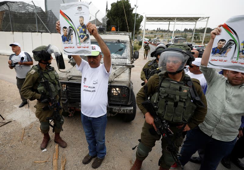 Israeli soldiers stand next to a journalist holding a poster of two Palestinian journalists that were killed recently in Gaza, during a protest demanding freedom of the press, near Ramallah, in the occupied West Bank