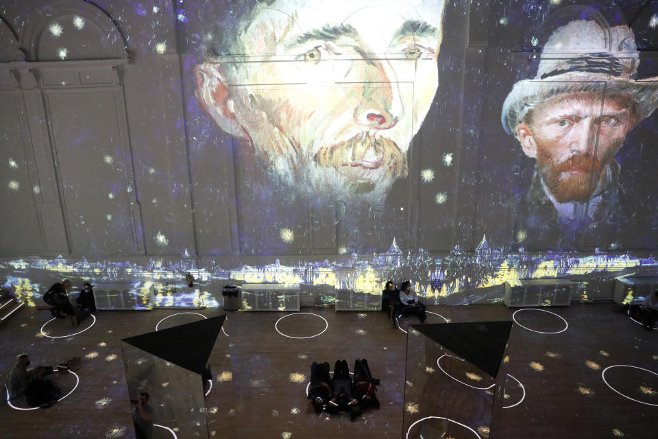 Patrons socially distance as they look at the moving images cast on the walls, floors and reflecting mirrors during a virtual display titled "Immersive Van Gogh" on Thursday, Feb. 18, 2021, at the Lighthouse ArtSpace, in Chicago. (AP Photo/Shafkat Anowar)