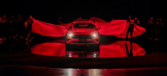 Ford pulling sheets off a Ford Mustang under red lighting at its China unveiling.