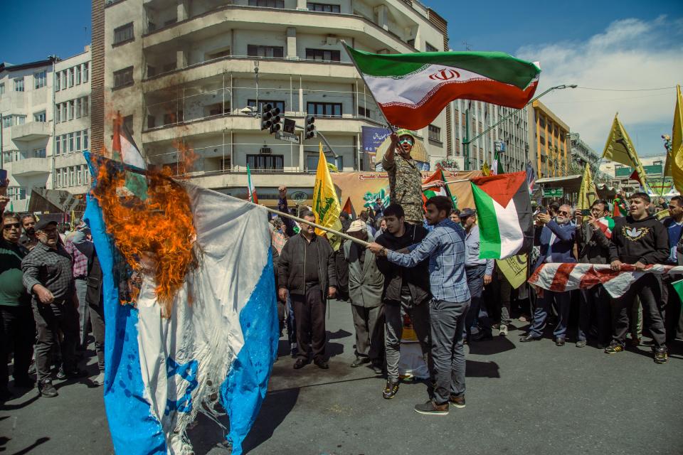 Iranian demonstrators burn a representation of the Israeli flag as one of them waves Iranian and Palestinian flags during an annual rally to mark Quds Day, or Jerusalem Day, in support of Palestinians, in Tehran, Iran, Friday, April 5, 2024. In the rally in Tehran, thousands attended a funeral procession for the seven Revolutionary Guard members killed in an airstrike widely attributed to Israel that destroyed Iran's Consulate in the Syrian capital on Monday. (Photo by Hossein Beris / Middle East Images / Middle East Images via AFP) (Photo by HOSSEIN BERIS/Middle East Images/AFP via Getty Images)