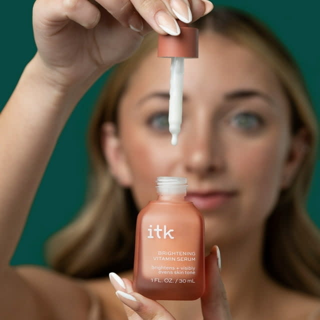 Woman holds a dropper and bottle of ITK brightening serum, focusing on the product