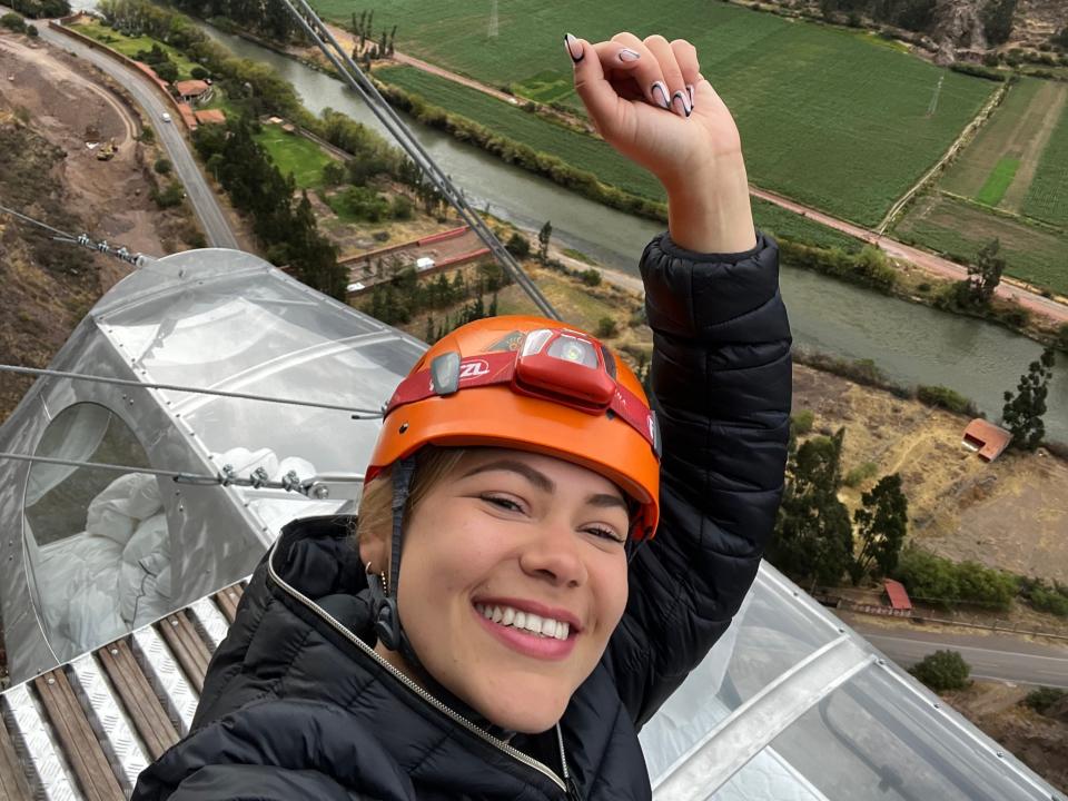 Victoria raises her hand over her head at the top of the climb. The hotel pod can be seen beneath her.