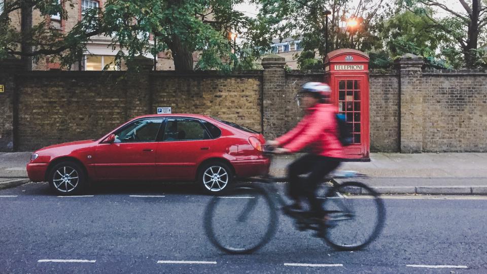  A cyclist riding next to a parked car and a telephone box 