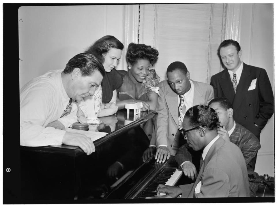 Jack Teagarden, Dixie Bailey, Mary Lou Williams, Tadd Dameron, Hank Jones, Dizzy Gillespie and Milt Orent crowd around a piano at Williams’ New York apartment in 1947.