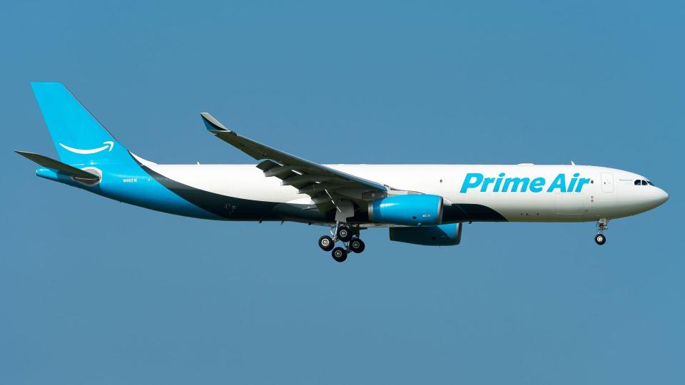 A light-blue tailed Amazon Prime Air jet on airport approach against blue sky.