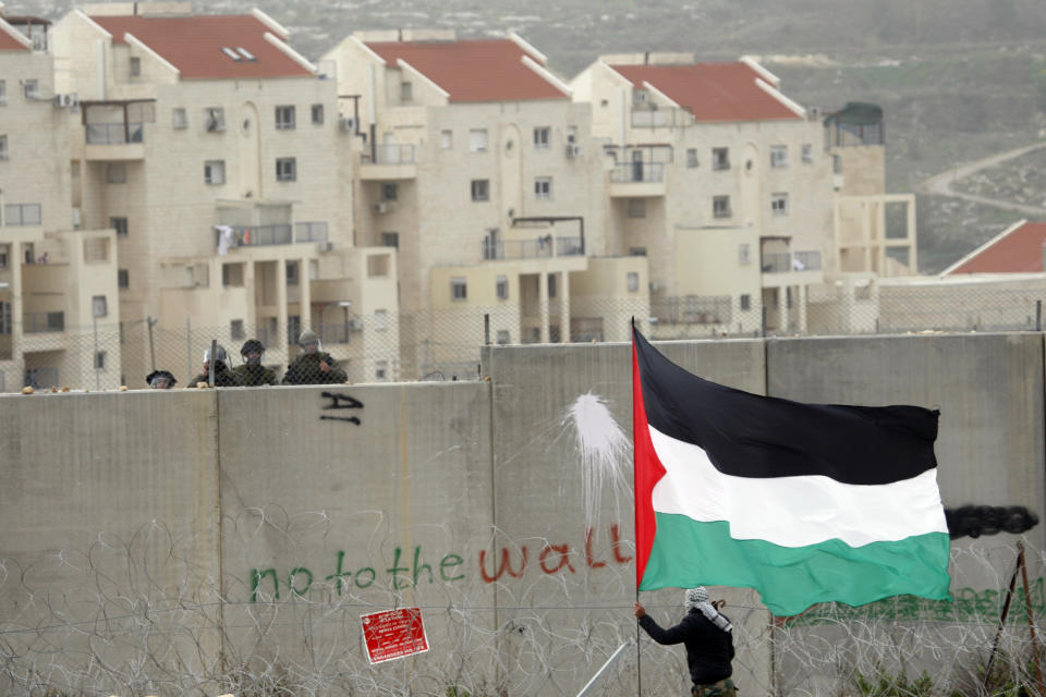 FILE- In this Friday, Feb. 17, 2012 file photo, the West Bank Jewish settlement of Modiin Illit rises in the background while a protestor waves a Palestinian flag in front of Israeli troops during a protest against Israel's separation barrier in the West Bank village of Bilin. Trump's self-proclaimed ‘’deal of the century' was anything but for the Palestinians' when it was released earlier this year, effectively greenlighting Israeli annexation in the occupied West Bank, killing off the two-state solution in an already moribund peace process and upending decades of official U.S. policy with regards settlements.(AP Photo/Majdi Mohammed, File)