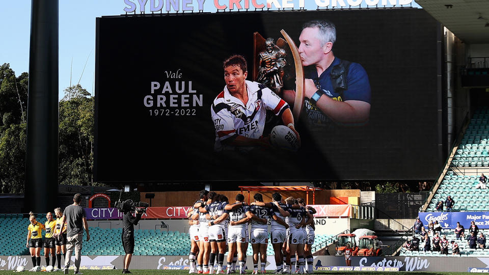 Cowboys players are seen huddled together beneath a screen displaying a tribute to Paul Green.