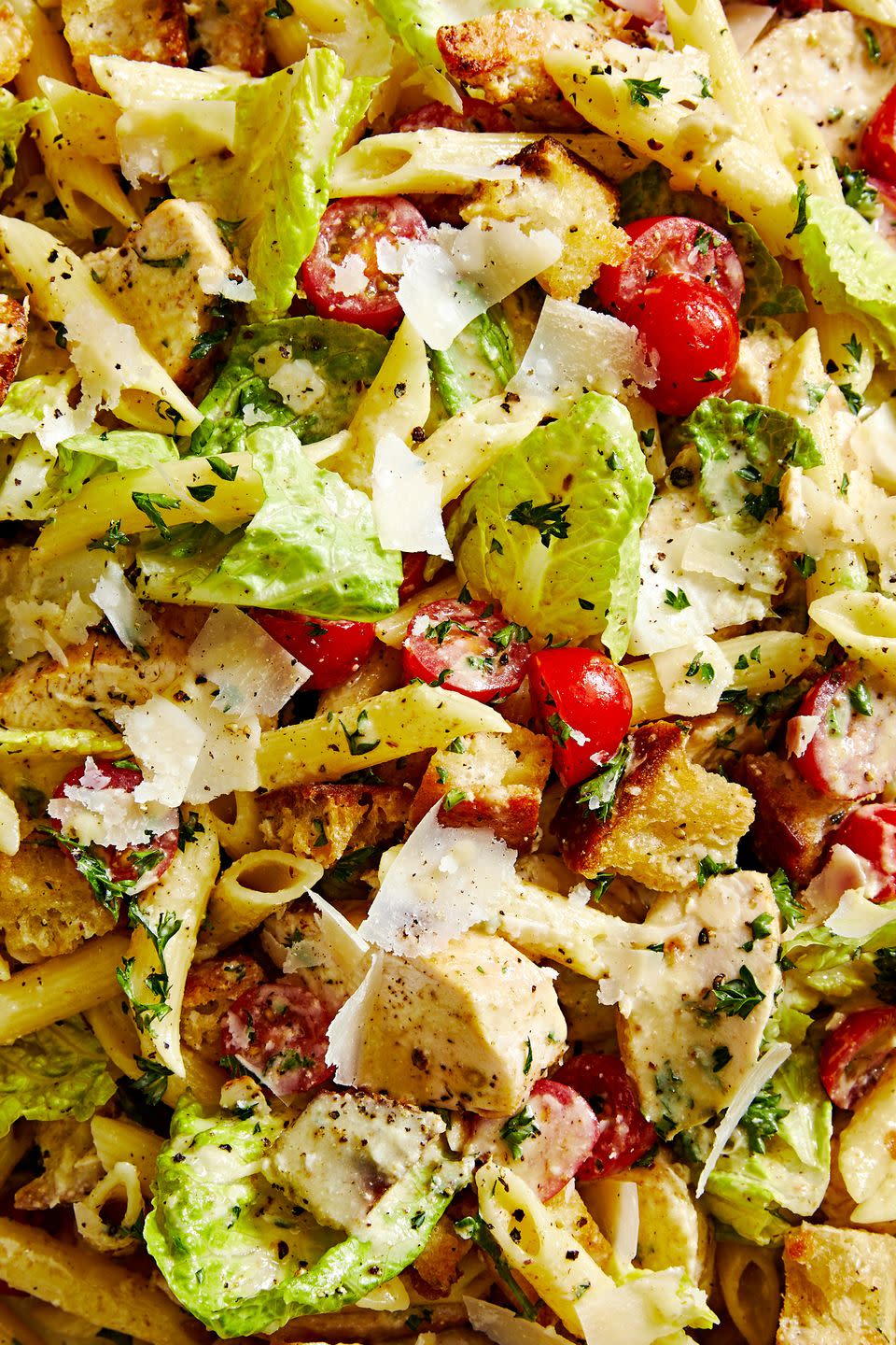 close up of chicken caesar pasta salad with romaine, halved cherry tomatoes, croutons, penne, and shave parmesan