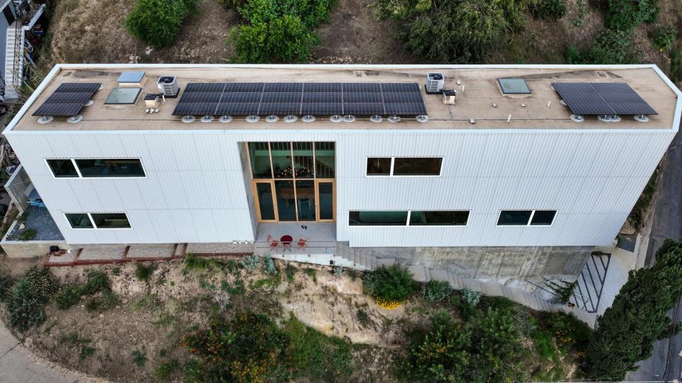 From above, you see the tall, skinny and long home with big vertical windows and solar panels on the roof.