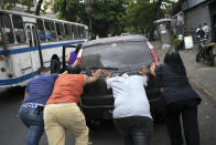 FILE - In this May 25, 2020 file photo, people push a car that ran out of gas to a state-run oil company PDVSA filling station during a fuel crunch in Caracas, Venezuela. With motorists waiting in lines to fill up their cars with gas that is increasingly scarce, the government proposed in Oct. 2020 to the Constitutional Assembly an “Anti-Blockade Law,” to get around U.S. sanctions. (AP Photo/Matias Delacroix, File)