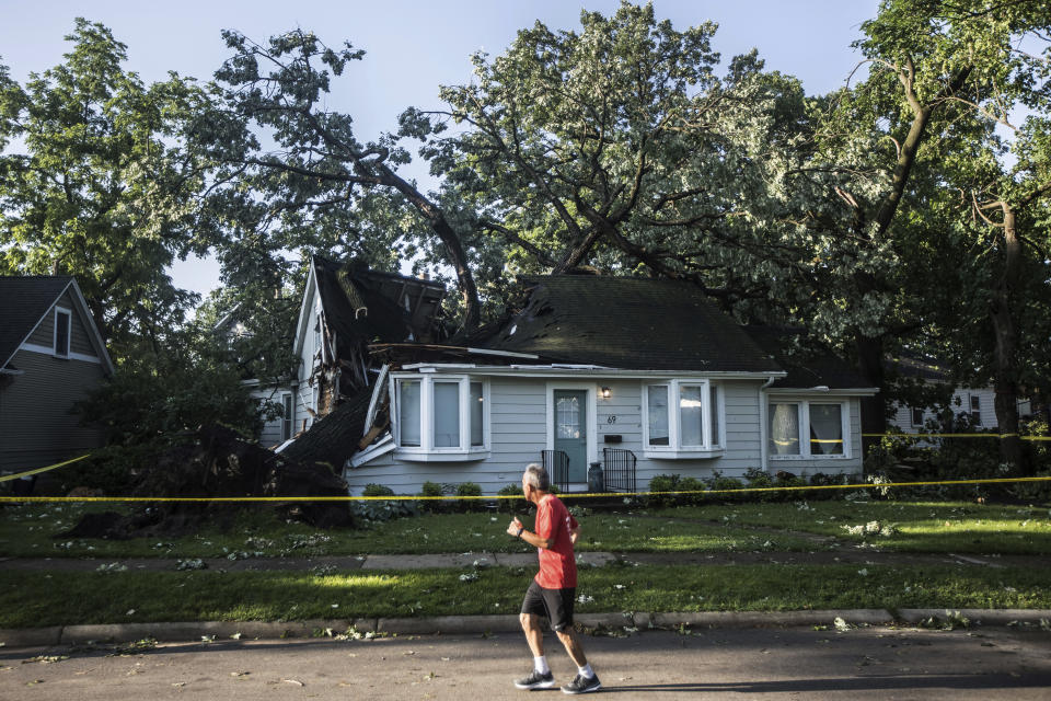 A person jogs past a large tree that fell into the roof of a home in Riverside during Monday evening's storm that raced across the Chicago area. A supercell thunderstorm with winds in excess of 80 mph (129 kph) toppled trees and damaged power lines Monday evening as it left a trail of damage across the Chicago area and into northwestern Indiana, the National Weather Service said. (Steven Rosenberg/Chicago Tribune via AP)