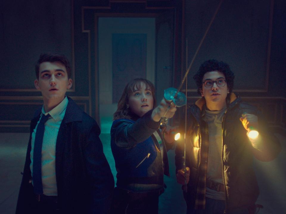 Three teens standing side by side in a dark room looking up at an unseen threat.