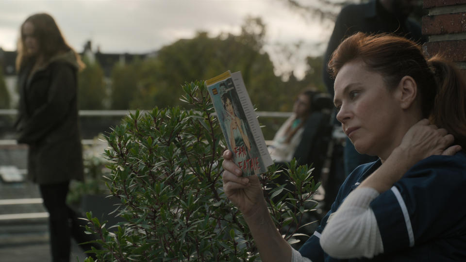 Nurse Mackenzie (Anna Friel) reading a book as Lina walks by in Locked In