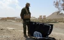 A member of the Syrian pro-government forces carries an Islamic State group flag as he stands on a street in the ancient city of Palmyra after troops recaptured the city from IS jihadists