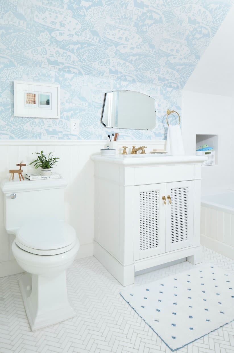 white bathroom with herringbone tile floor, wainscoting, pale blue and white scenic paper on upper walls and sloped ceiling