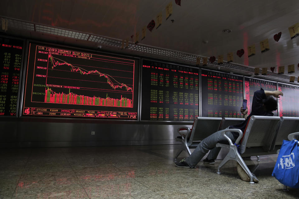 A man browses his smartphone in front of an electronic board displaying stock prices at a brokerage house in Beijing, Thursday, Aug. 16, 2018. Asian shares are falling as investors fret over slowing economic growth, especially in China. Technology stocks and oil and metals prices skidded overnight on Wall Street. (AP Photo/Andy Wong)