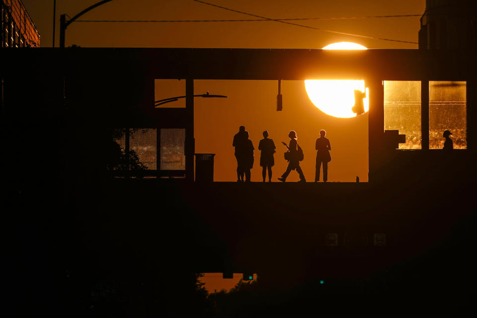 Commuters waiting for Chicago's L Train are silhouetted against the setting sun at Addison Station, Monday, Sept. 19, 2022, in Chicago. (AP Photo/Kiichiro Sato)