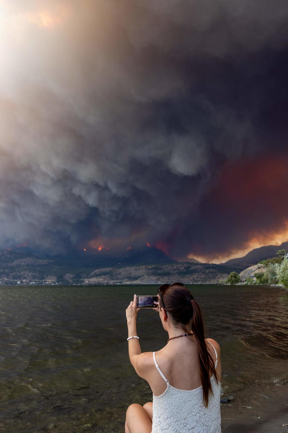 Residents watch the McDougall Creek wildfire in West Kelowna, British Columbia, Canada, on August 17, 2023, from Kelowna. Evacuation orders were put in place for areas near Kelowna, as the fire threatened the city of around 150,000. Canada is experiencing a record-setting wildfire season, with official estimates of over 13.7 million hectares (33.9 million acres) already scorched. Four people have died so far. (Photo by Darren HULL / AFP) (Photo by DARREN HULL/AFP via Getty Images)