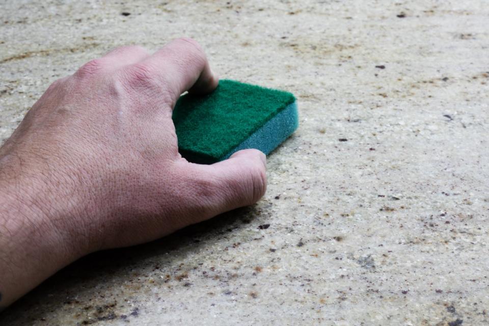 A man cleaning a granite counter with a sponge.