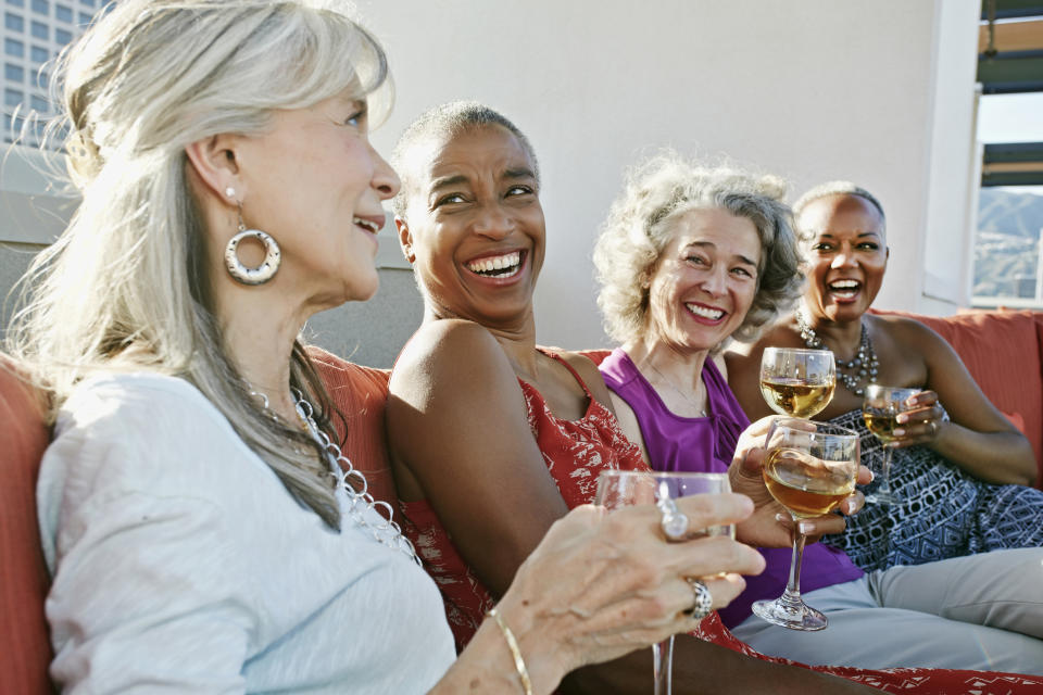 Four joyful women are sharing a toast with wine glasses, seated together on a couch, depicting a moment of friendship and celebration