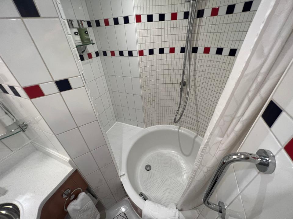 A round, white bathtub with a ledge, tiled walls, a showerhead,  and a shower curtain. 