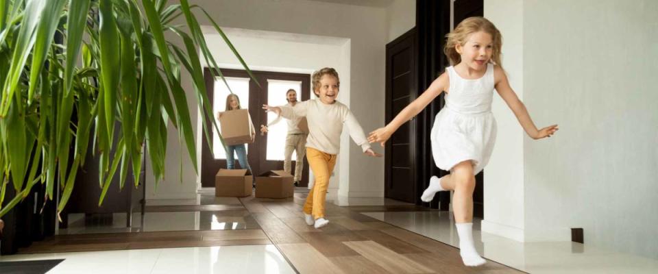 Happy young family with cardboard boxes in new home at moving day concept, excited children running into big modern home